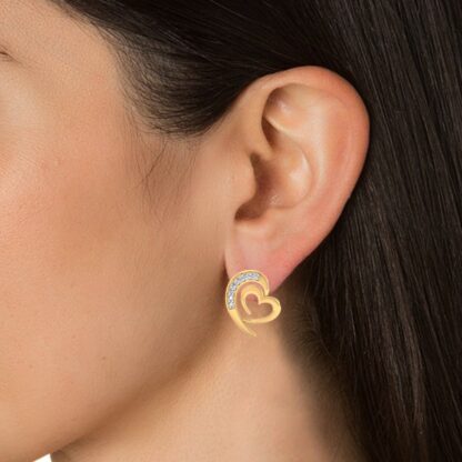 Close-up of yellow gold diamond arc heart stud earring worn on a model's ear